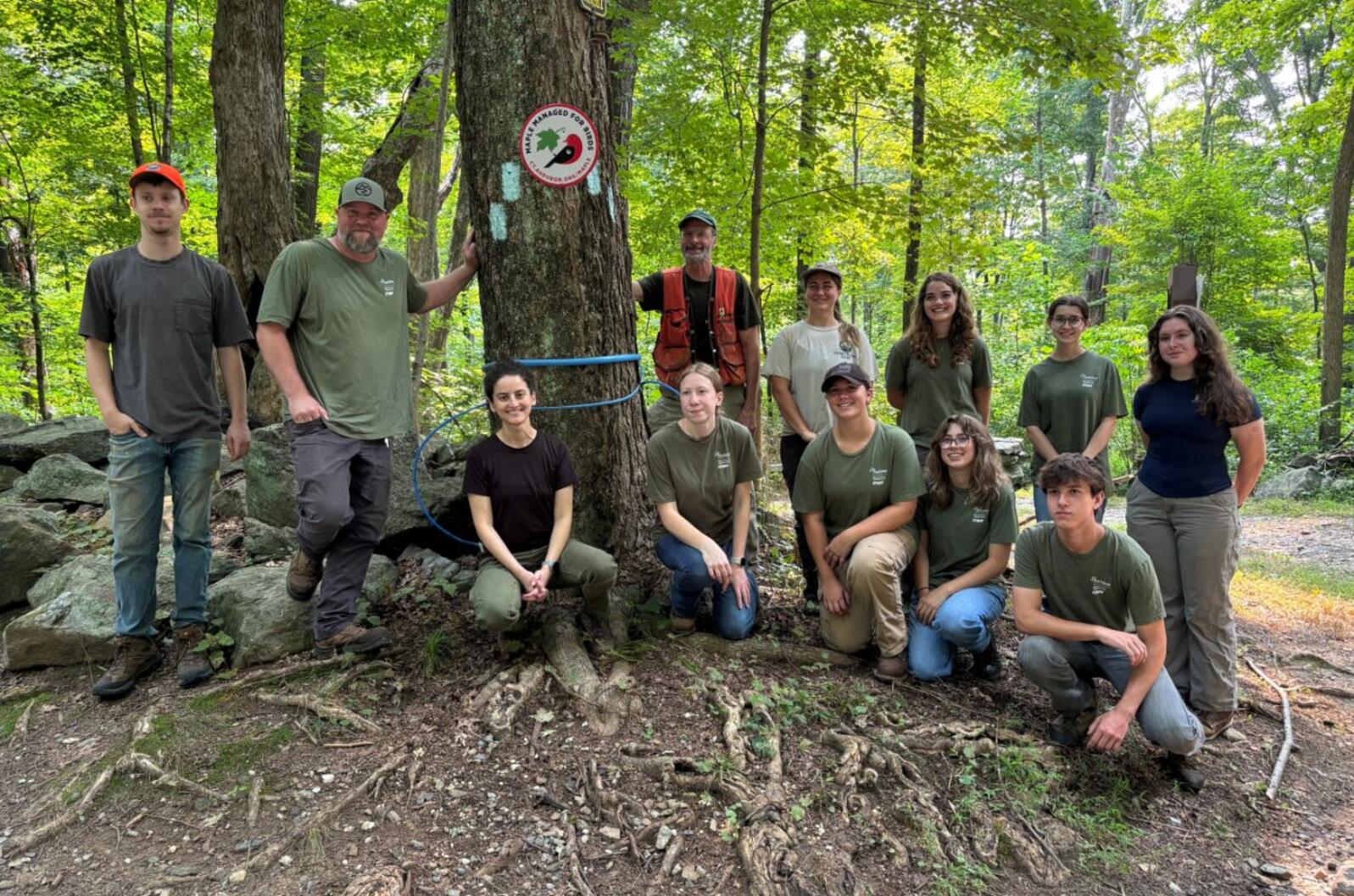 Group of teenagers pose with staff in front of a sign for the bird-friendly maple program