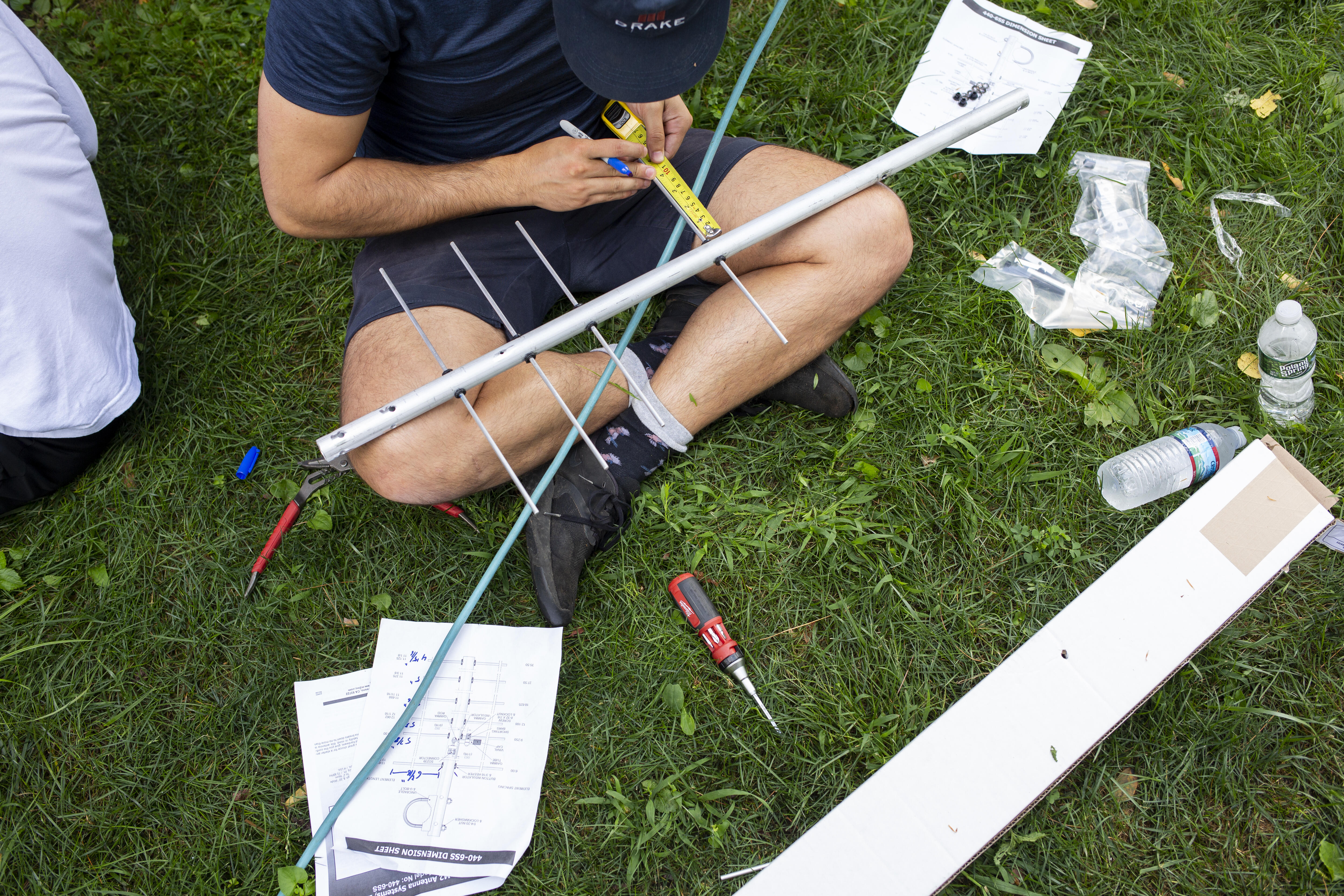 A man sits on the ground, measuring antennae with a measuring tape.